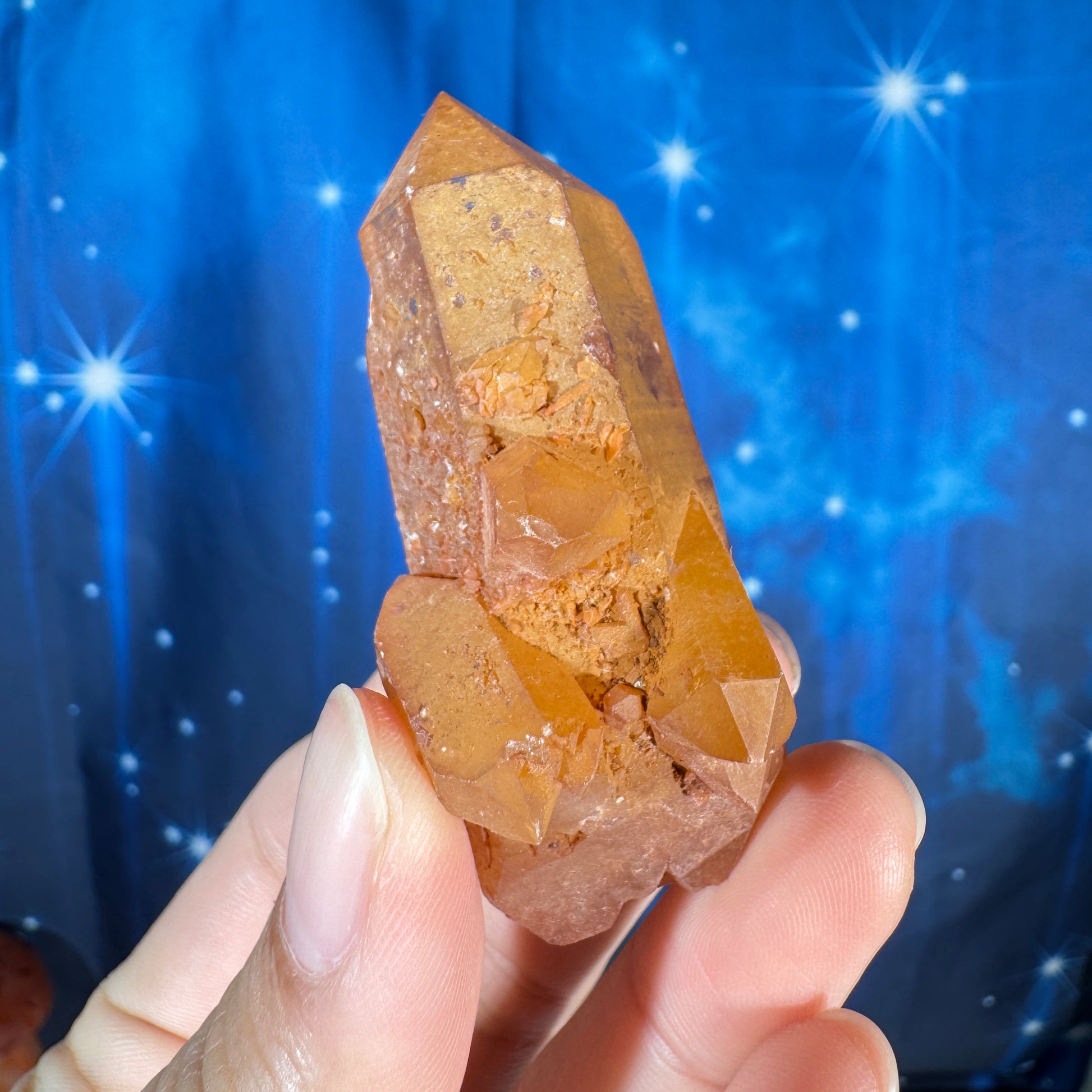 Hand holding a crystal against a blue background with star-like lights