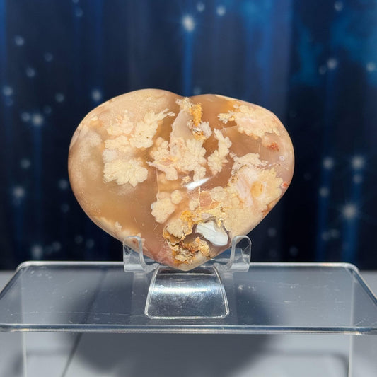 May include: A heart shaped agate with a white and orange pattern. The agate is on a clear stand.