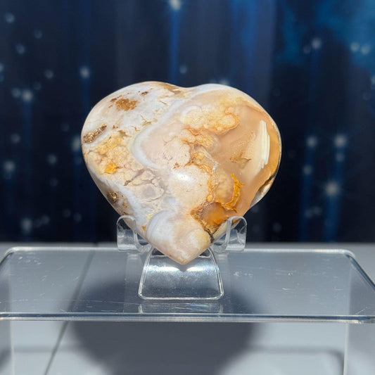May include: A heart-shaped agate crystal with white and orange swirls and patterns. The crystal is on a clear stand.